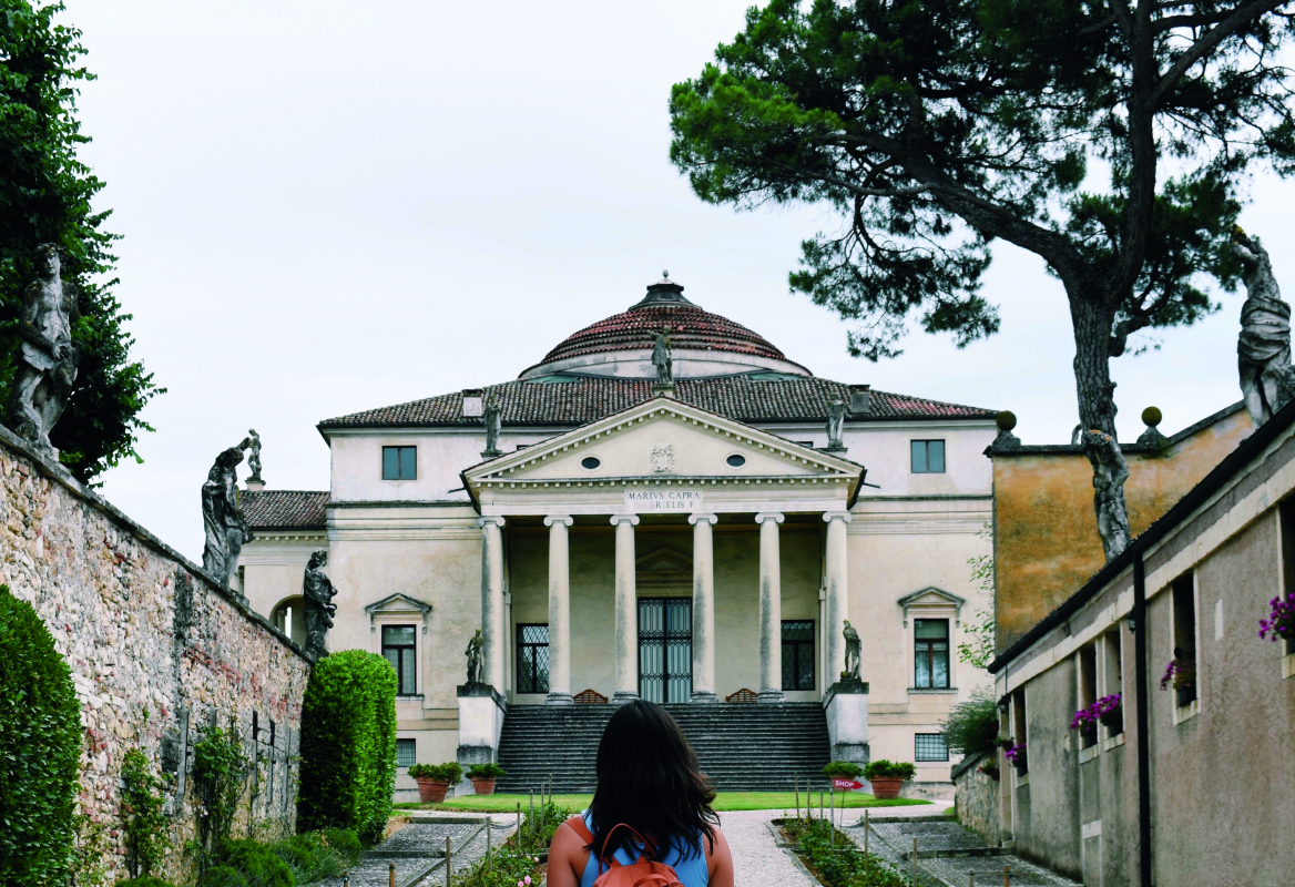 A student walks up a long path towards an Italian architectural site.