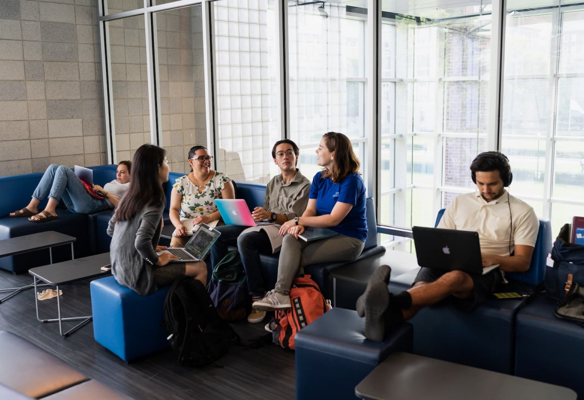 students gather on blue couches in Lerner Hall, in front of a glass wall.