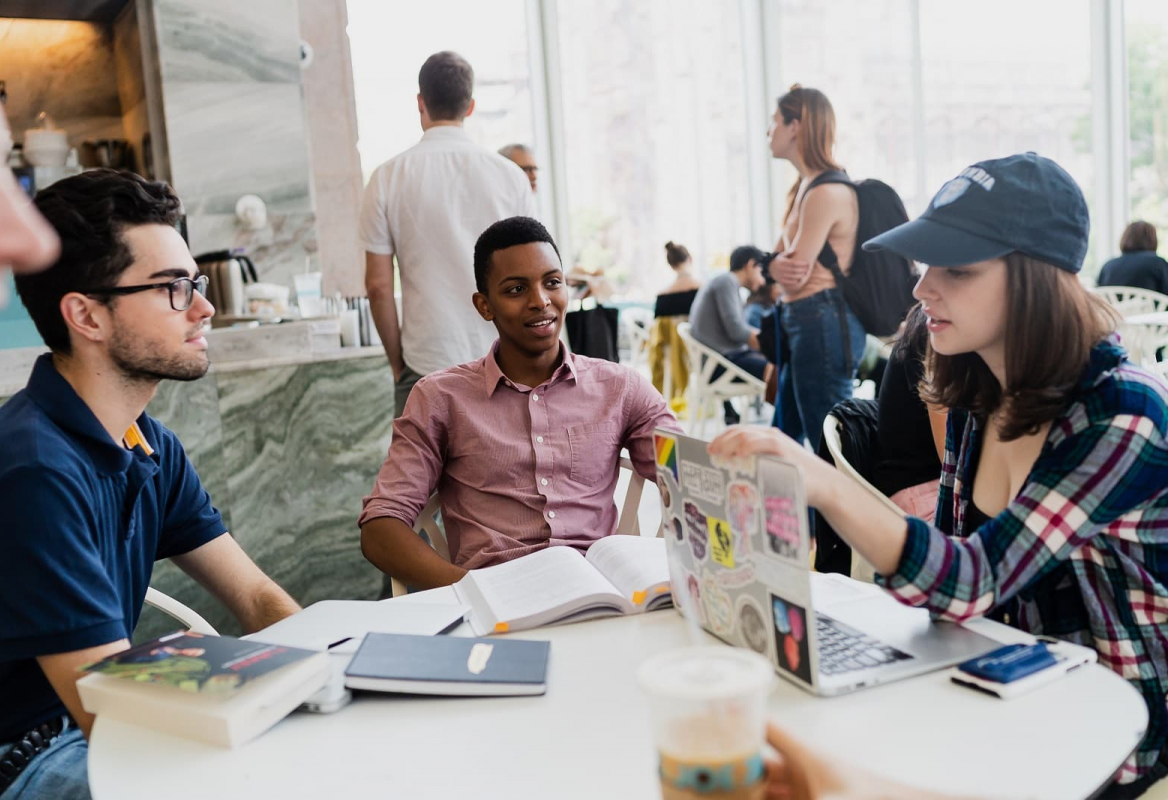 students sit around a table at a coffee shop with laptops and books