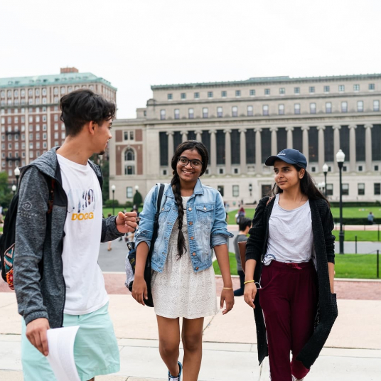 Three students walk across Low Plaza in conversation