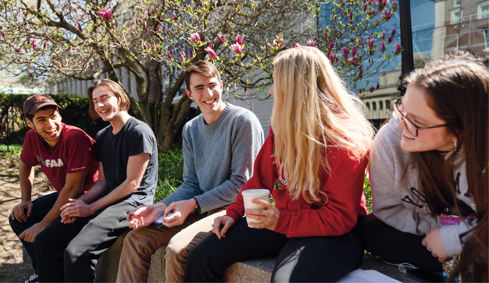 five students sitting on wall outside and laughing