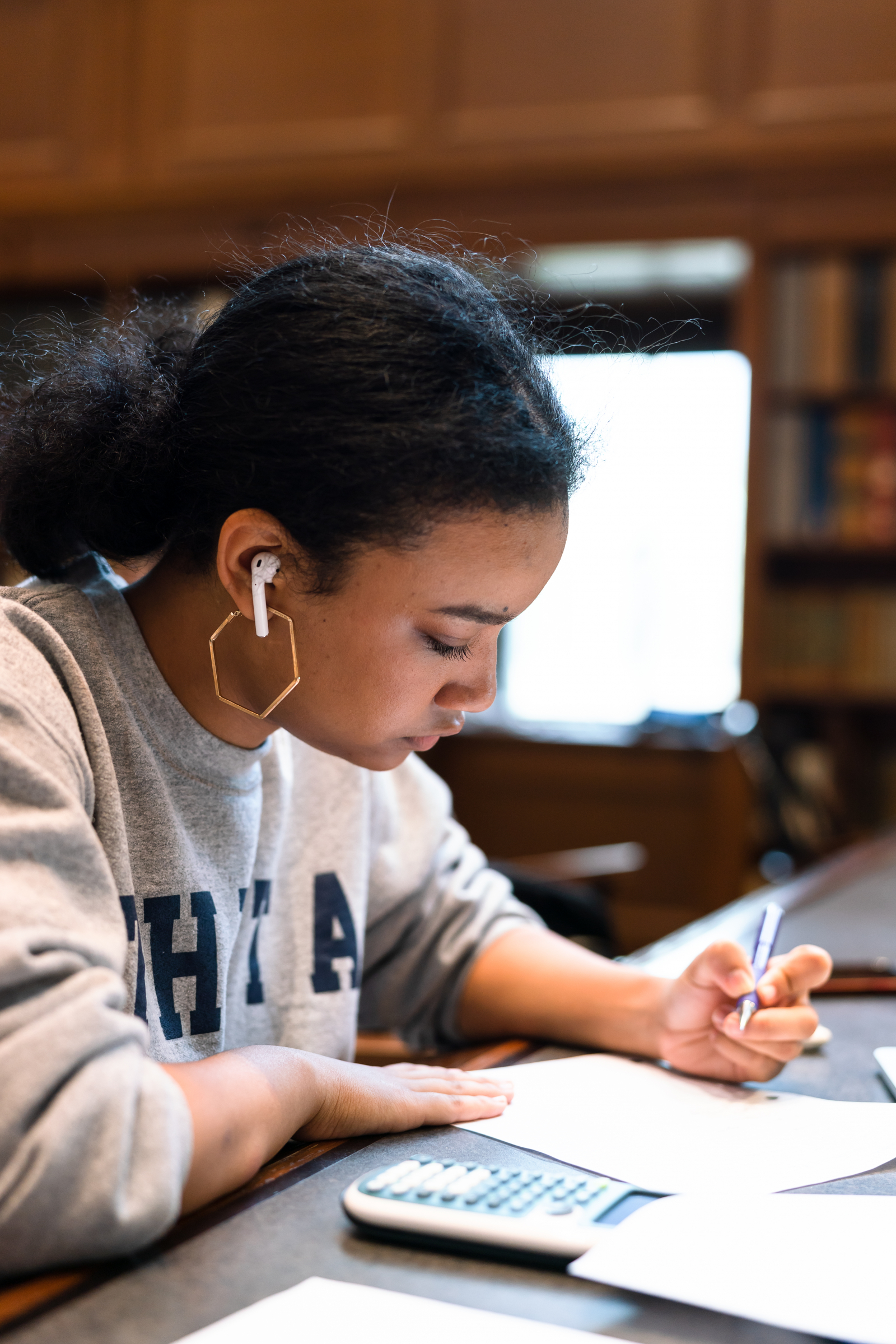 Student sits at a desk in the library with headphones in studying.