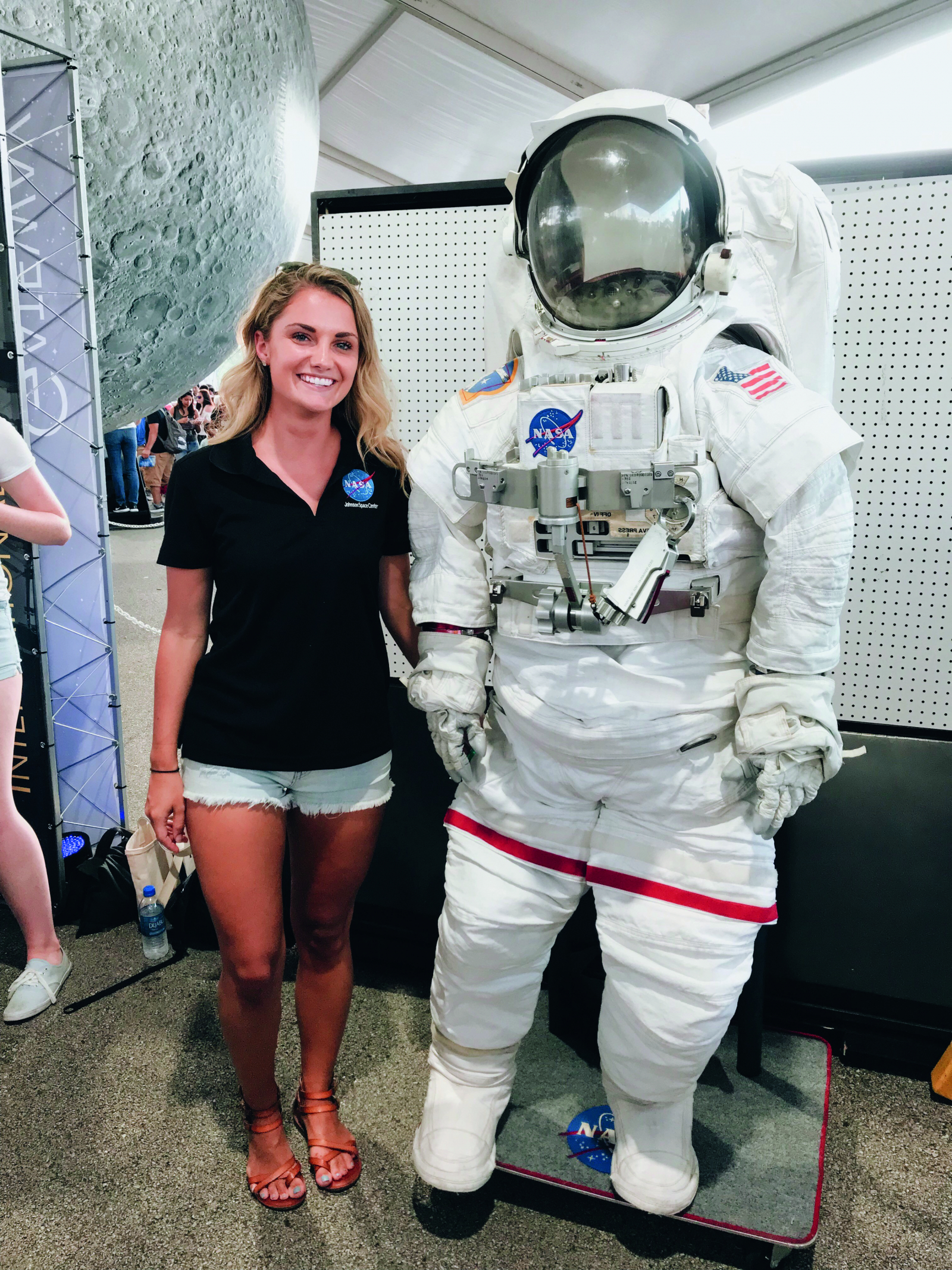 Young female student stands next to an empty astronaut suit in a space museum.