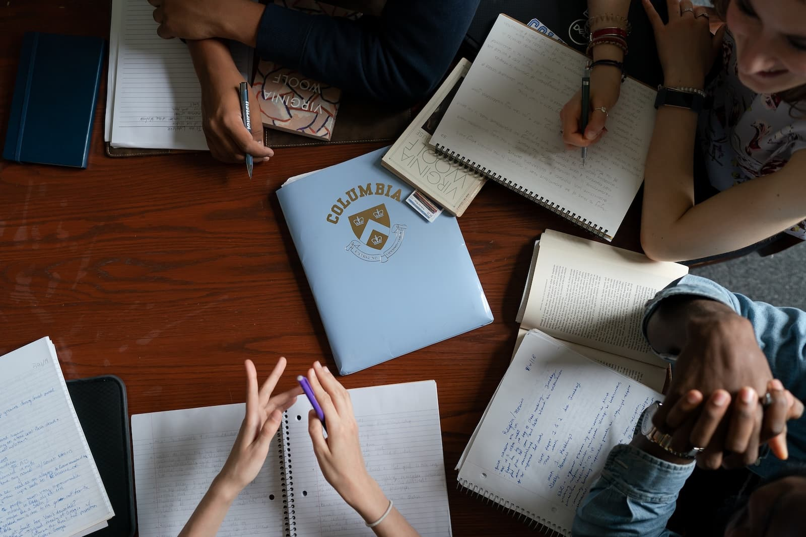 Students discuss over notebooks on a table