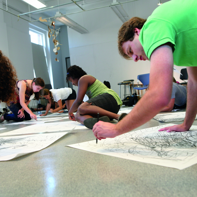 Students sketching on paper on a classroom floor