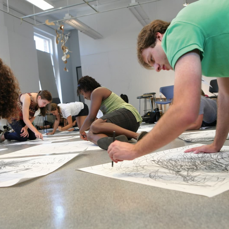 Students sketching on paper on a classroom floor