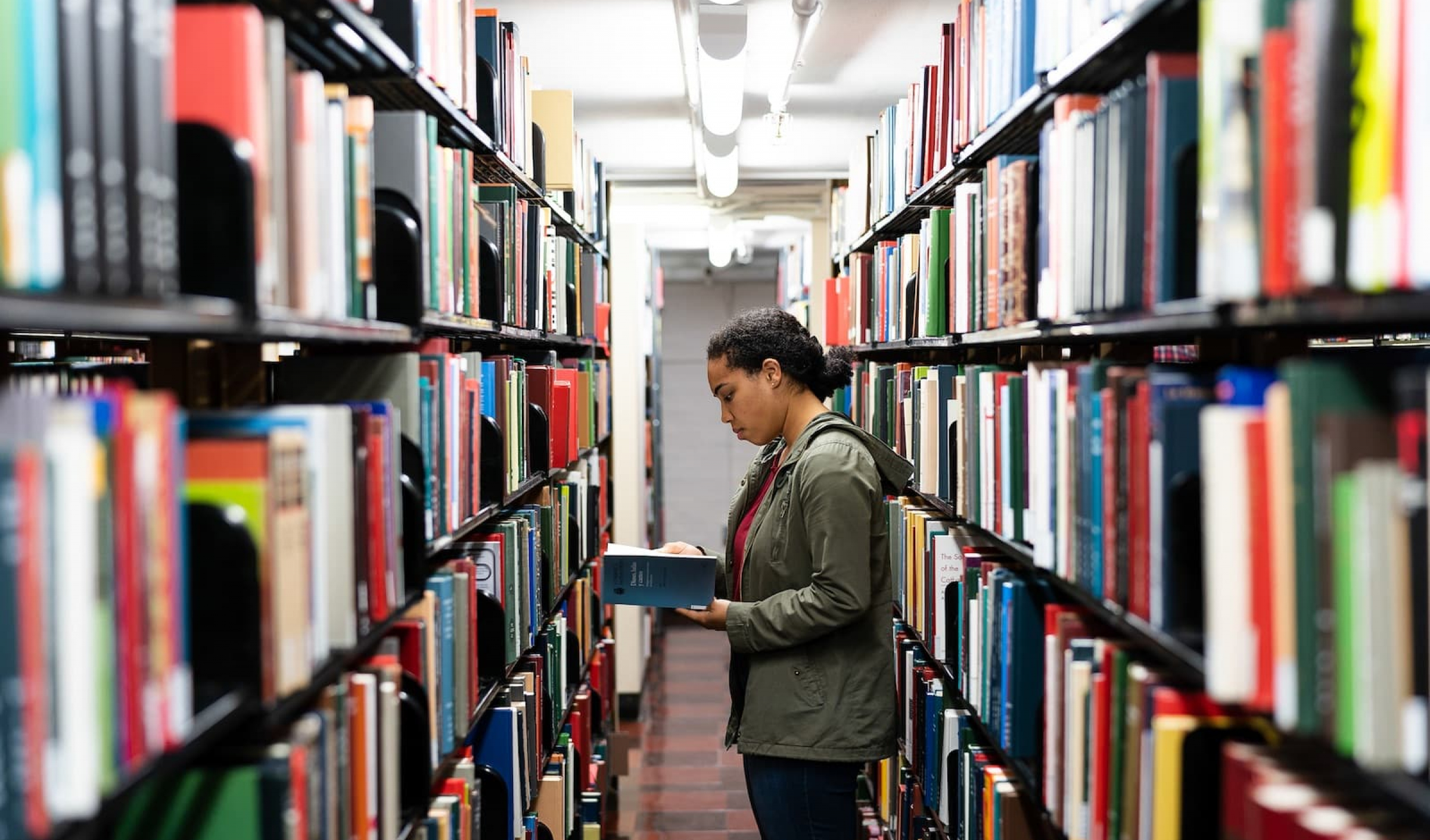student looking at books in the library stacks