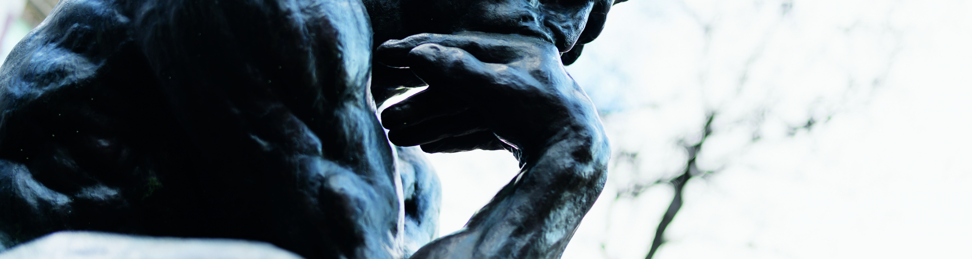 A statue of a man is crouched over, eyes gazing downward, with his hand brought to his chin. He is the thinker.