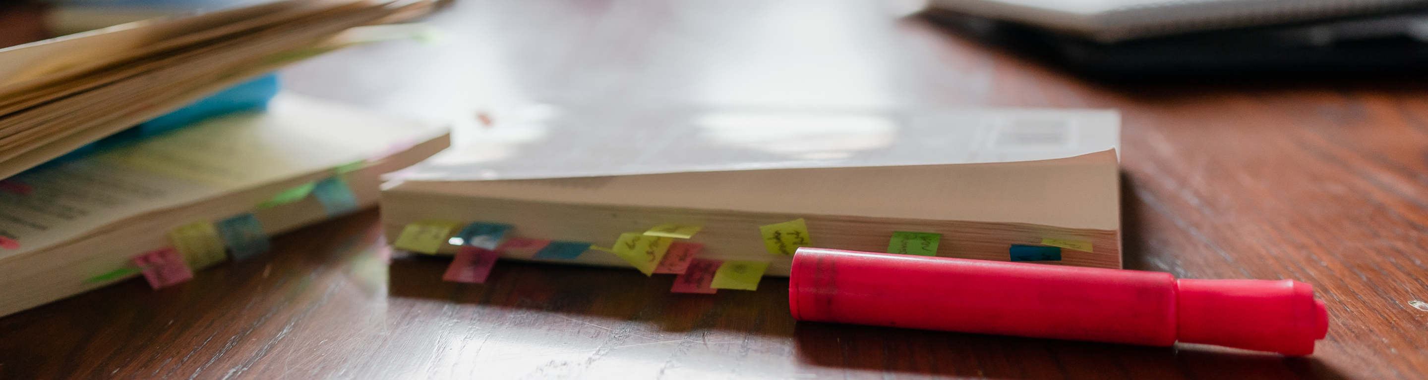 A closeup of a wooden table with a highlighter and multiple books.