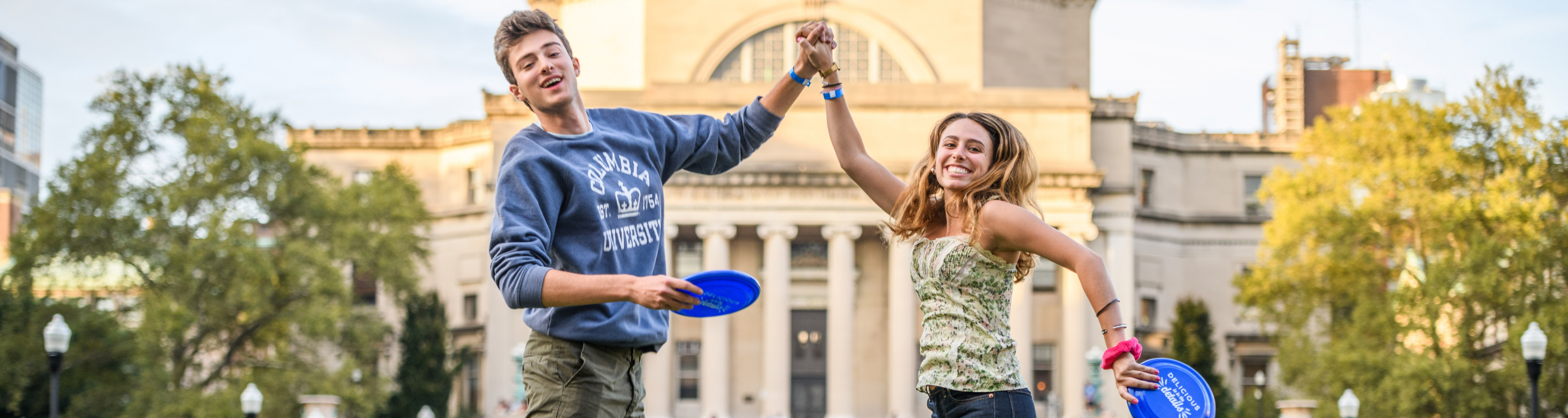 Students hold hands and frisbees on South Lawn in front of Low Library