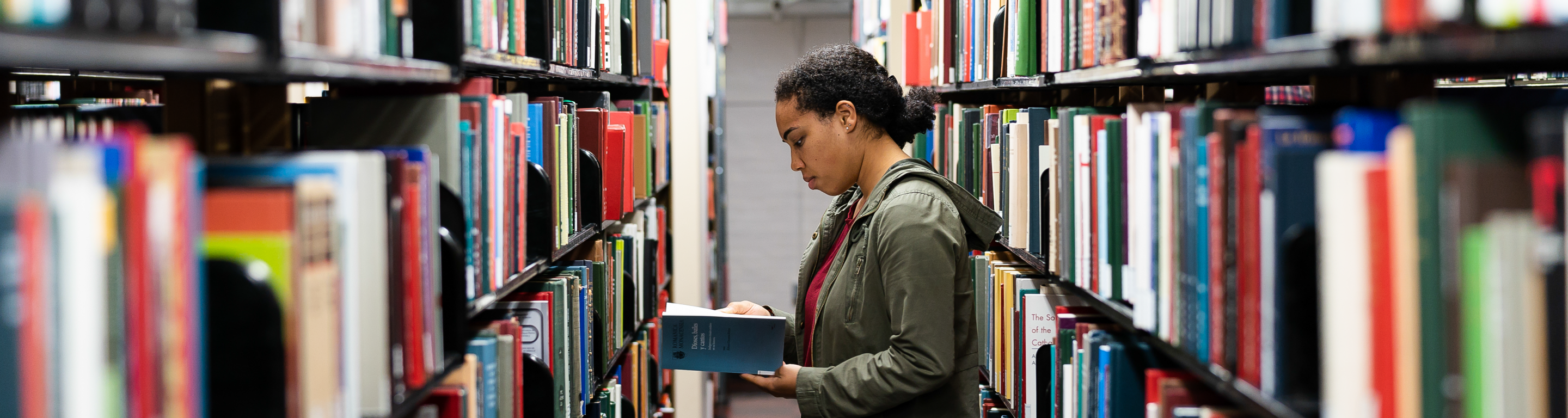 student looking at books in the library stacks