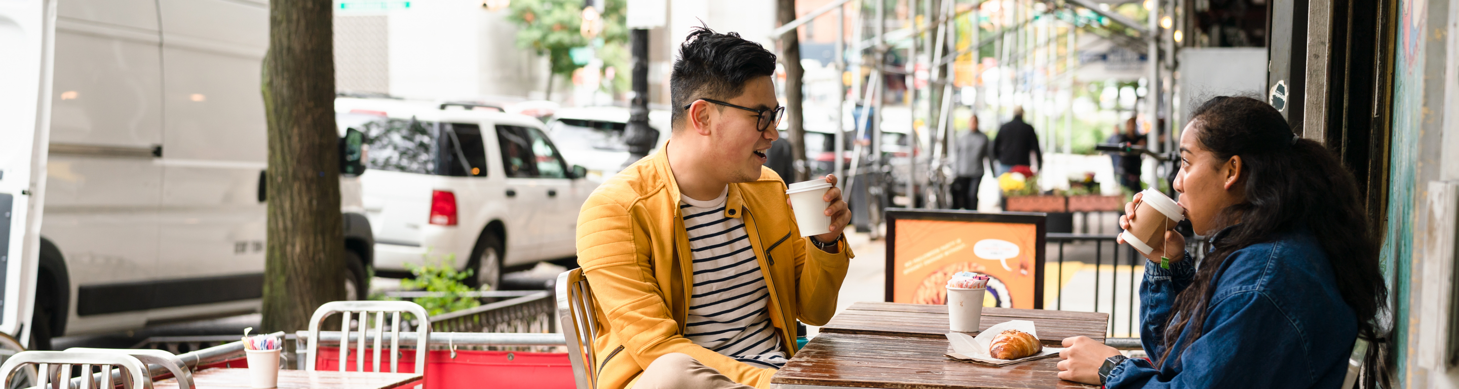 Two students sit outside at a cafe and drink coffee while talking