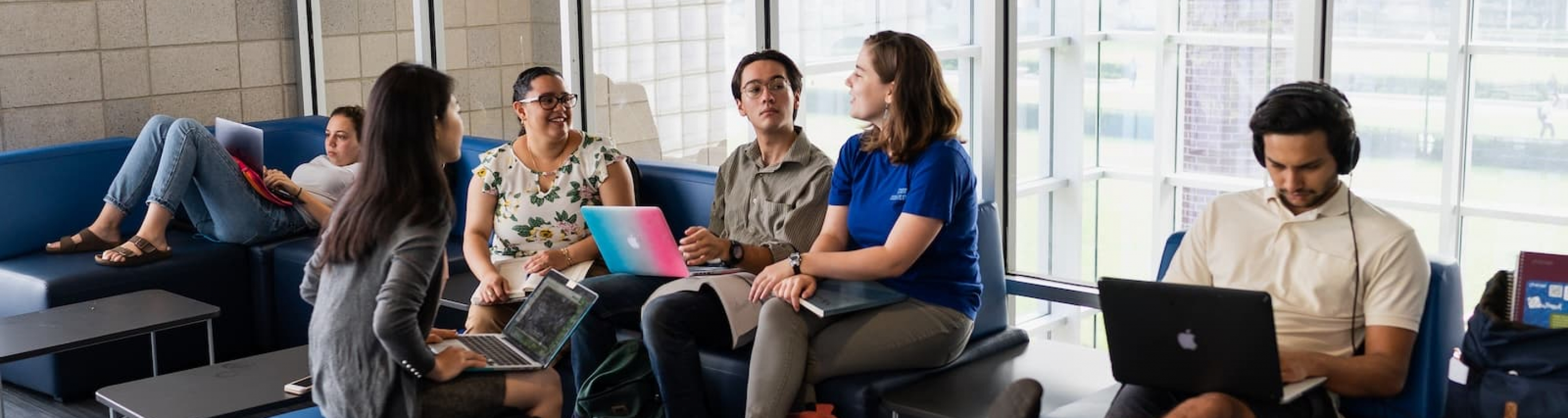 students gather on blue couches in Lerner Hall, in front of a glass wall. 