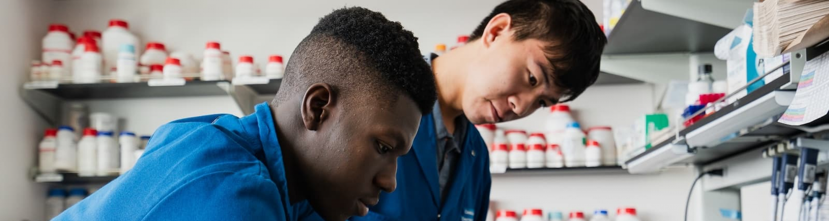 Two students in lab coats and gloves work together in a research lab