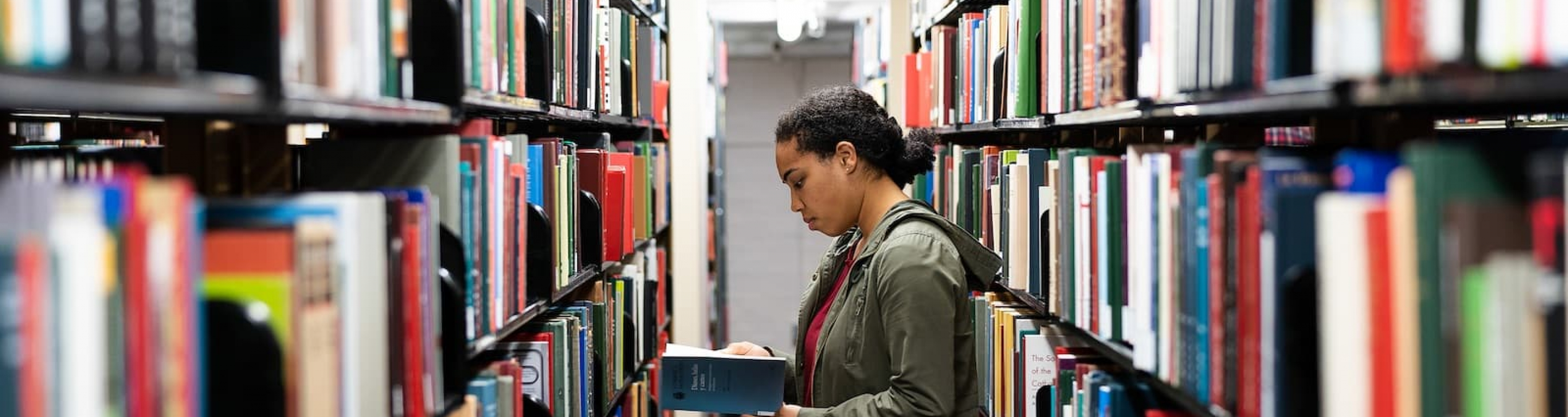 student looking at books in the library stacks
