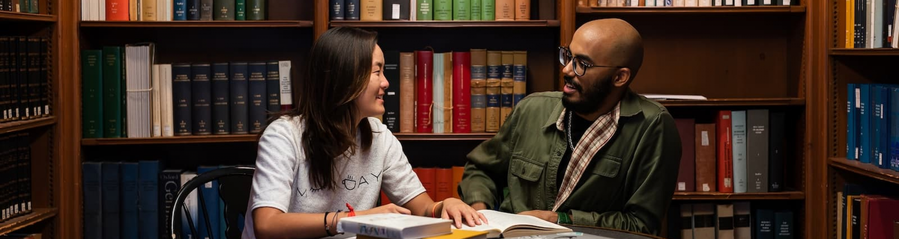 Two students studying at a table surrounded by bookshelves