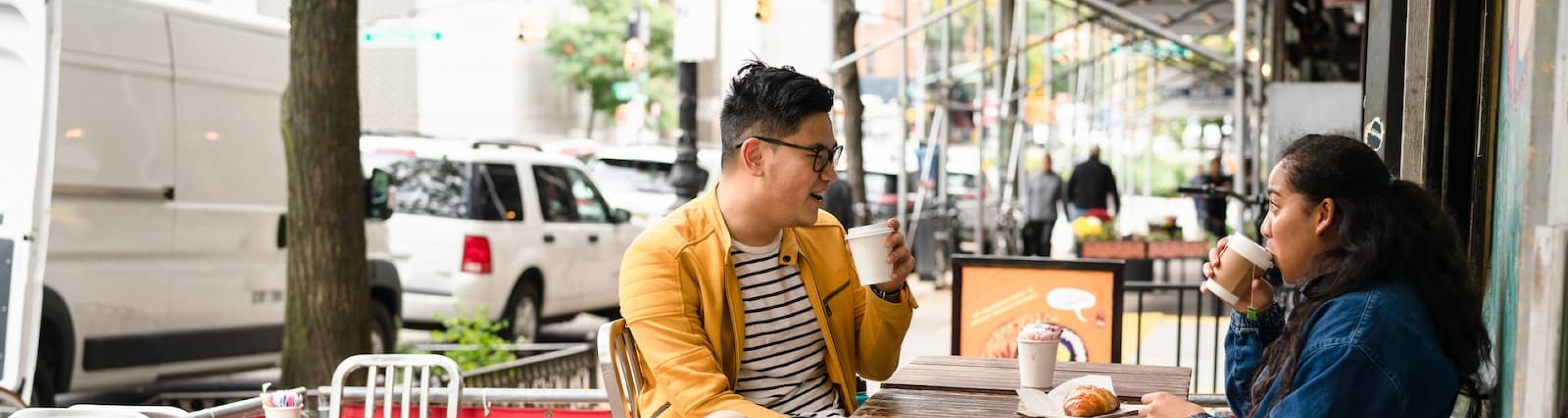 Two students sit outside at a cafe and drink coffee while talking