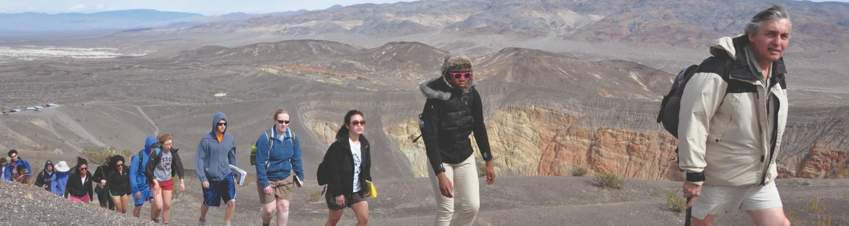 A line of students treks up a rocky, desert path with a professor in front.