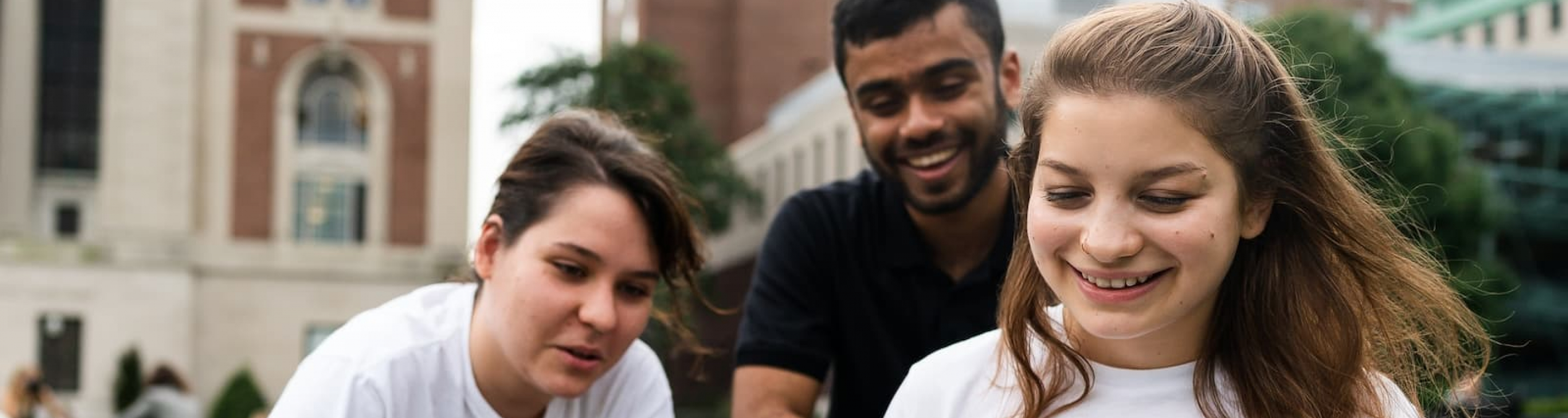 Students sitting on Butler lawn looking at a computer and smiling