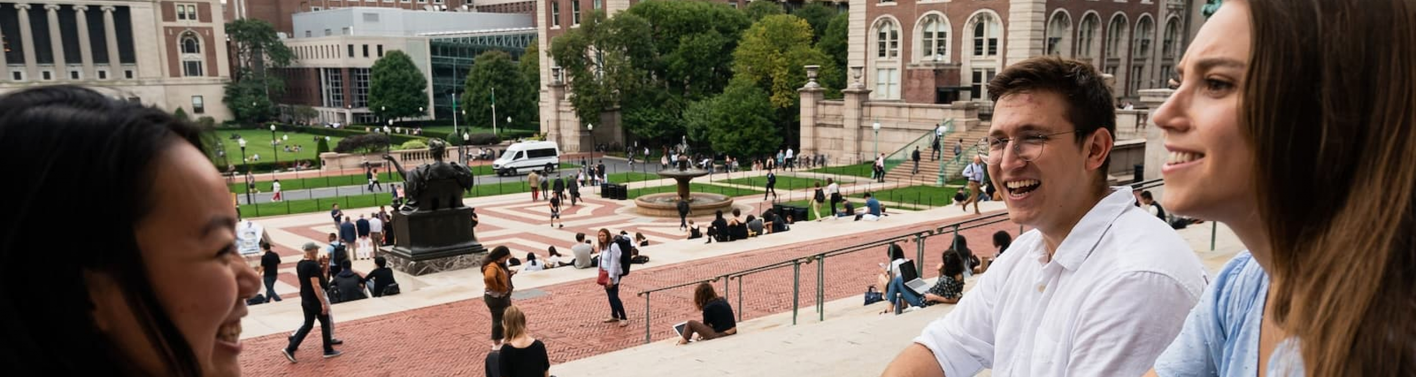 Three students talking on Low steps overlooking campus behind them