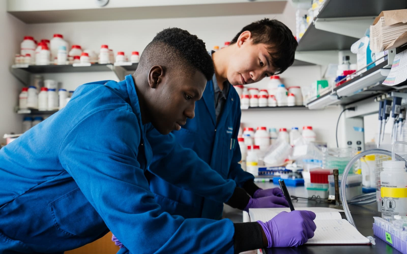 Two students in lab coats and gloves work together in a research lab
