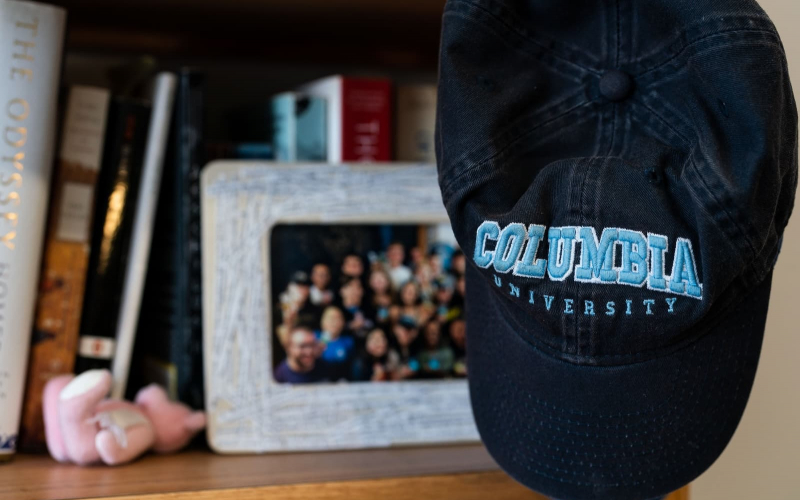 a navy Columbia baseball cap sitting on a gray photo frame. The frame is on a wooden desk. 