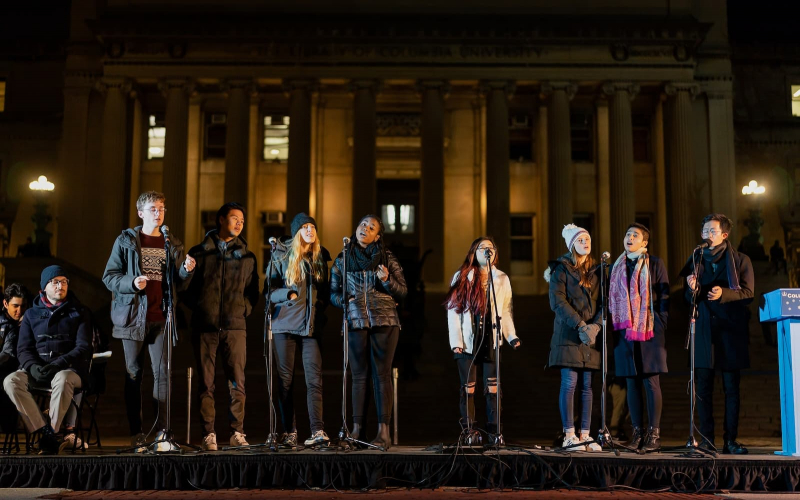 A group of a cappella singers perform on a winter night in front of Low Library. 