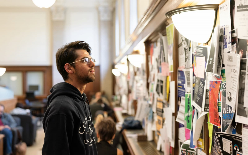 a student staring at a bulletin board covered in flyers