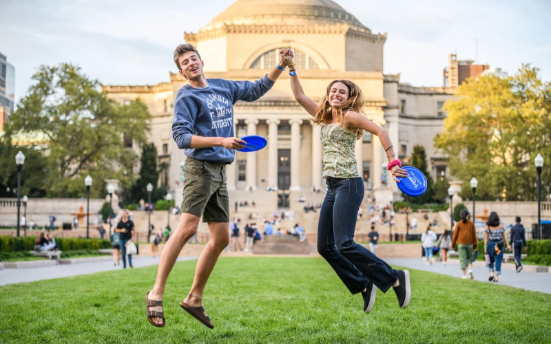 Students hold hands and frisbees on South Lawn in front of Low Library